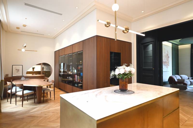 Cuisine élégante mêlant noyer, laiton et pierre naturelle. Ambiance chaleureuse et design haut de gamme avec îlot central et salle à manger intégrée.